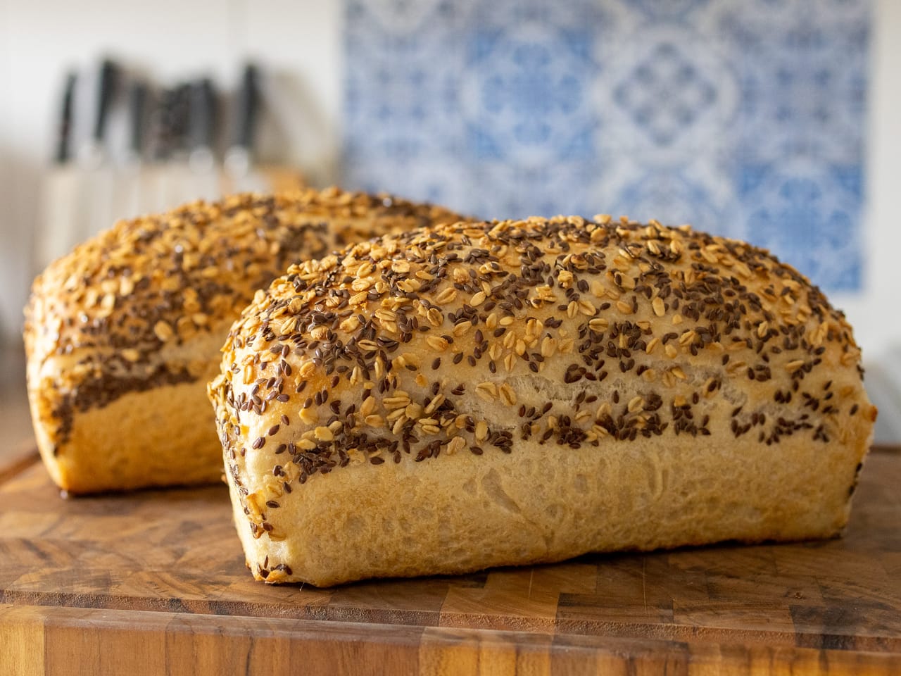 Two sourdough pan loaves topped with oats and flax seeds on a wooden board