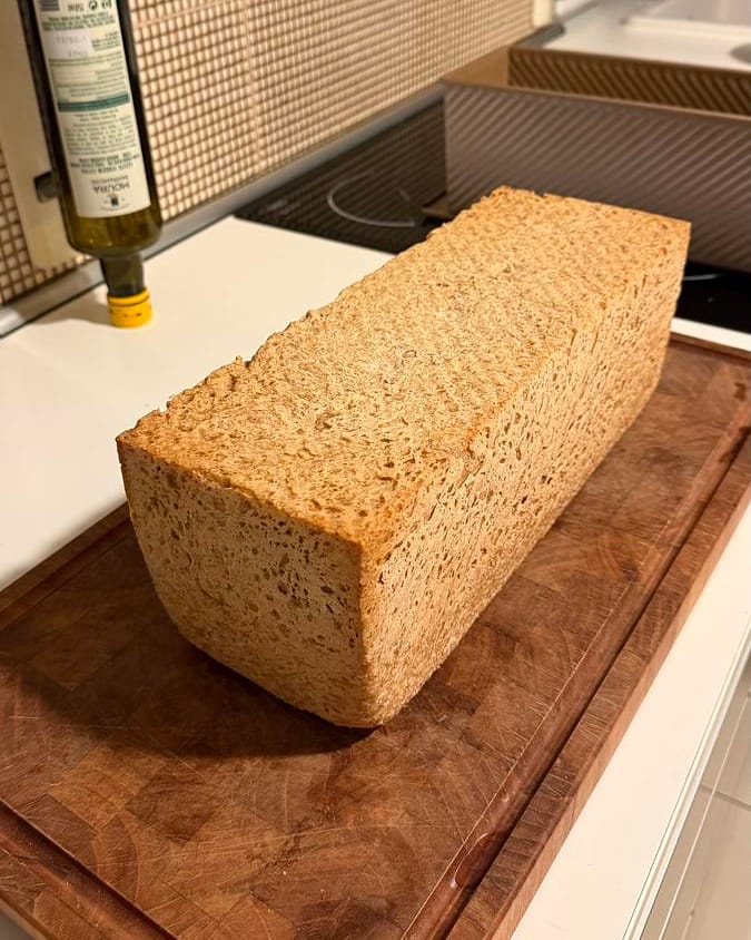 A square whole wheat sandwich loaf out of its pan on a wooden board